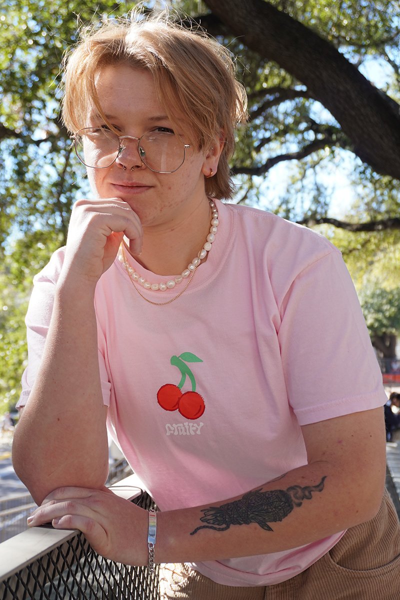 Cherry Fruity Shirt Lean Against Fence Outside Light Pink T-Shirt Subtle Gay Pride Queer Fashion LGBTQ Clothing Inclusive Apparel